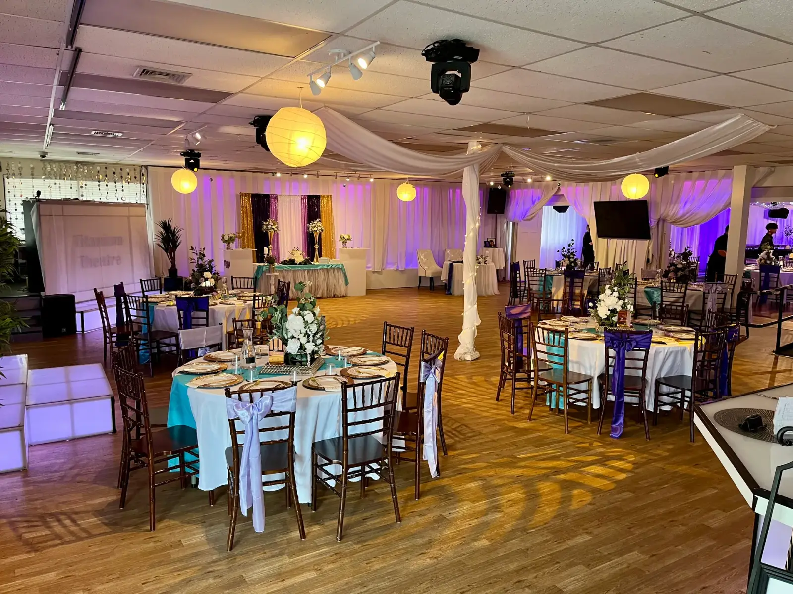 The Titanium Theatre ballroom set for an event with draped ceilings, chiavari chairs, an LED dance floor, and purple uplighting